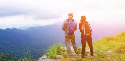 pareja de excursionistas con mochila de pie en la cima de la montaña con destellos de luz solar, cielo azul, nube blanca y niebla en doi luang tak, tailandia - vista del paisaje, belleza de la naturaleza y punto de referencia para el turista foto