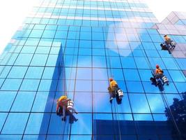 Bangkok, Thailand - October 16, 2017 Group of cleaner hanging, washing and cleaning windows on high rise building with orange sunlight flare - High building and Risk working. photo