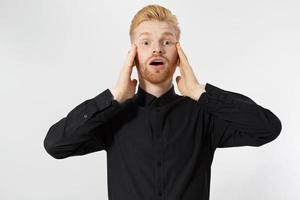 Portrait of shoked red-hair male groom realizes that he forgot to buy rings, dressed in black shirt with white bowtie, stares at camera with stupefied expression, isolated over blank copy space photo