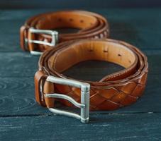 two leather brown belts on dark wooden background photo