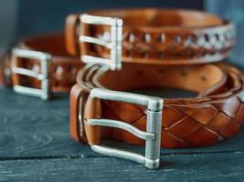 three leather brown belts on dark wooden background photo