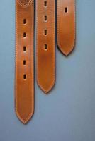 three leather brown belts on grey paper background photo