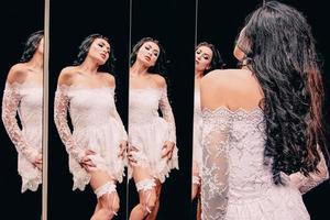 Portrait of beautiful brunette woman in white shoes and white dress standing near the mirrors photo