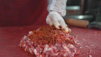 un cuoco che lavora la carne. kebab di adana. lo chef che aggiunge la salsa piccante all'adana kebab. fare l'adana kebab con salsa piccante video