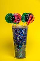 multi-colored lollipops in a blue glass on a yellow background. photo