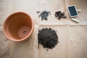 Shot of materials for gardening at home. Pot, soil, pebbles and tomato seeds. Brown paper as background photo