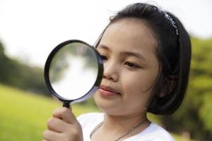 Asian little girl holding a magnifying glass in outdoor photo