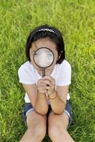 Asian little girl holding a magnifying glass in outdoor photo