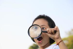 Asian little girl holding a magnifying glass in outdoor photo