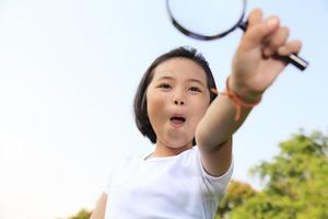 Asian little girl holding a magnifying glass in outdoor photo