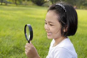 Asian little girl holding a magnifying glass in outdoor photo