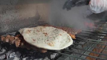 o mestre coloca pita na carne cozida na grelha. a carne é cozida no carvão. espetos de carne, kebab de adana, asas de frango e legumes. video
