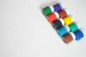 Closed jars with gouache of different colors standing in a row on a white background. Hobby, drawing, painting. photo