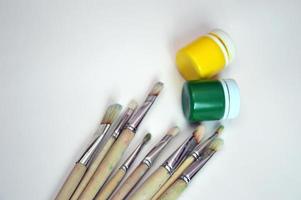 A set of brushes with wooden handles and bristle bristles lying with cans of gouache yellow and green paint on a white background. Place for text. photo