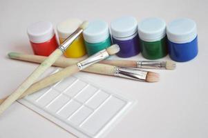 Multi-colored gouache paint in closed jars and a set of artistic brushes. Drawing materials, hobbies, tools, artist's palette. photo