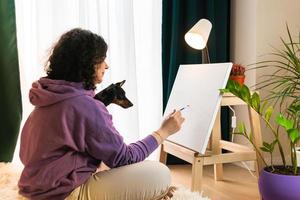 The adult woman painting by numbers indoors, her pet miniature pincher near. People with pets. photo