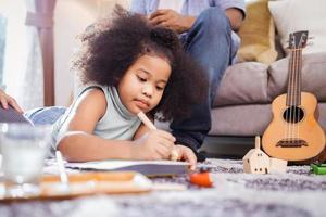 African American kid girl drawing with watercolors in the living room at home photo