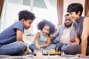 Two African American kids with mother and father playing chess in living room at home photo