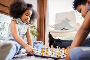 African American girl and boy playing chess on the floor in the living room at home photo