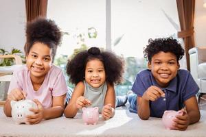Portrait of African American kids saving money in a piggy bank in living room at home photo