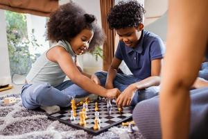 Funny African American children playing chess in the living room at home
