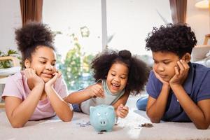 Happy African American Children saving money in a piggy bank together in living room at home photo