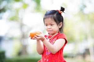 Portrait cute Asian kid girl holding oranges fruit. Chinese New Year concept. Child wear red qipao cheongsam. Children are 4 years old. photo