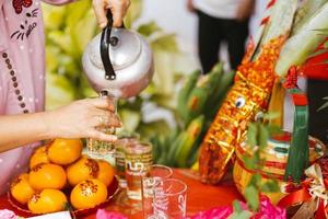 Kamphaeng Phet Thailand-14 Jan 2022. Hand person holding teapot, pouring tea full of glass. Orange fruit stick with auspicious letters that mean double happiness. photo