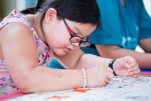 Portrait cute 6 year old Asian girl wearing eyeglasses. Kid is drawing picture of her imagination in classroom art class. photo