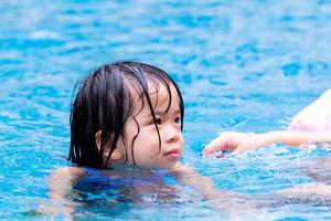 retrato lindo niño asiático niña jugando en la piscina azul claro. los niños disfrutan haciendo ejercicio en el agua. niño de 4 años está mojado. foto