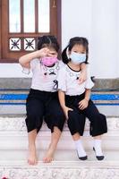 Portrait imaged kids 5 years old. Two cute girls wearing white face masks, children hugging each other's necks. Child smile brightly. Vertical photos. Sisters love each other. photo