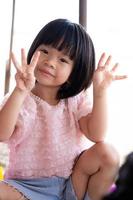 Portrait of child 4-5 year old. Cute Asian girl smiling sweetly looking at camera. Kid holds up four fingers on one side of three fingers to pose for photo. Vertical image. photo