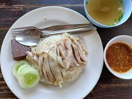 Hainanese chicken rice eat with chicken soup and sauce on a wooden background photo