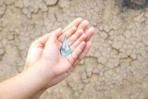 manos del día mundial del agua esperando el mundo en forma de gota de agua en el suelo árido de fondo. elementos de esta imagen proporcionada por la nasa. foto