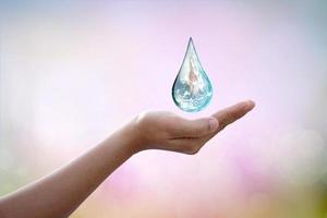 World Water Day Hands waiting for the world in water drop shape on background blurred flowers and sky with the light of the sun. Elements of this image furnished by NASA. photo