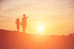 Mother encouraged her daughter out of the shadows at sunset. photo