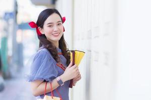 Asian beautiful woman in a gray Qipao dress with a red bow is smiling, holding a fan on the street in Chinatown, Thailand. photo