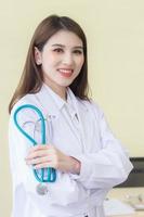 Young beautiful  Asian woman doctor Standing with arms crossed happy and smile in hospital. Wearing a white robe and stethoscope photo