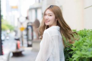 Asian woman with bronze hair turn s around in white shirt while walks on street. photo