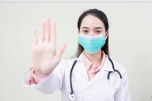 Asian woman doctor shows hand as stop sign which she wears medical clothing and medical face mask in  health care,pollution PM2.5,new normal and coronavirus protection concept. photo