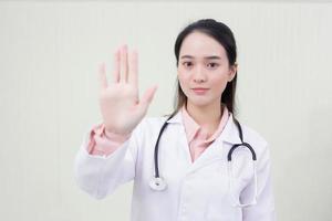 Asian beautiful woman doctor shows hand as stop sign which she wears medical clothing in  health care,new normal and coronavirus protection concept. photo