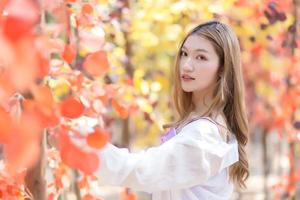 Asian beautiful woman who has long bronze hair stands and smiles happily with orange forest orange leave as background. photo