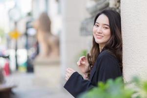 Asian long-haired woman in a dark blue robe is looking out and standing outdoors waiting for something in town. photo