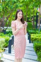 Asian professional  business female with long hair is smiling in the garden while looking at the tablet in her hand, work from anywhere concept. photo
