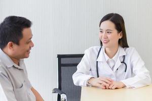 Young Asian professional woman doctor good mood smile suggests health solutions to elderly male patients in the hospital examination room. photo