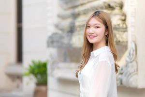 Portrait Asian beautiful girl with long bronze hair in white long sleeve shirt stand smile in an urban outdoor park. photo