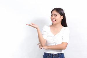 Asian beautiful woman in black long hair wears white shirt stands smiling and pointing up to present something on a white background. photo