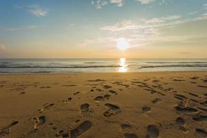 las huellas se mostraron en la arena en el mar y la puesta de sol con el cielo azul. foto