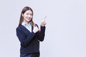 Asian working woman who has long hair wears black formal suit with blue shirt while she shows point up to present something on white background. photo