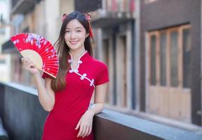 Beautiful Asian woman in red dress stands holds a fan among old city center in Chinese new year theme. photo